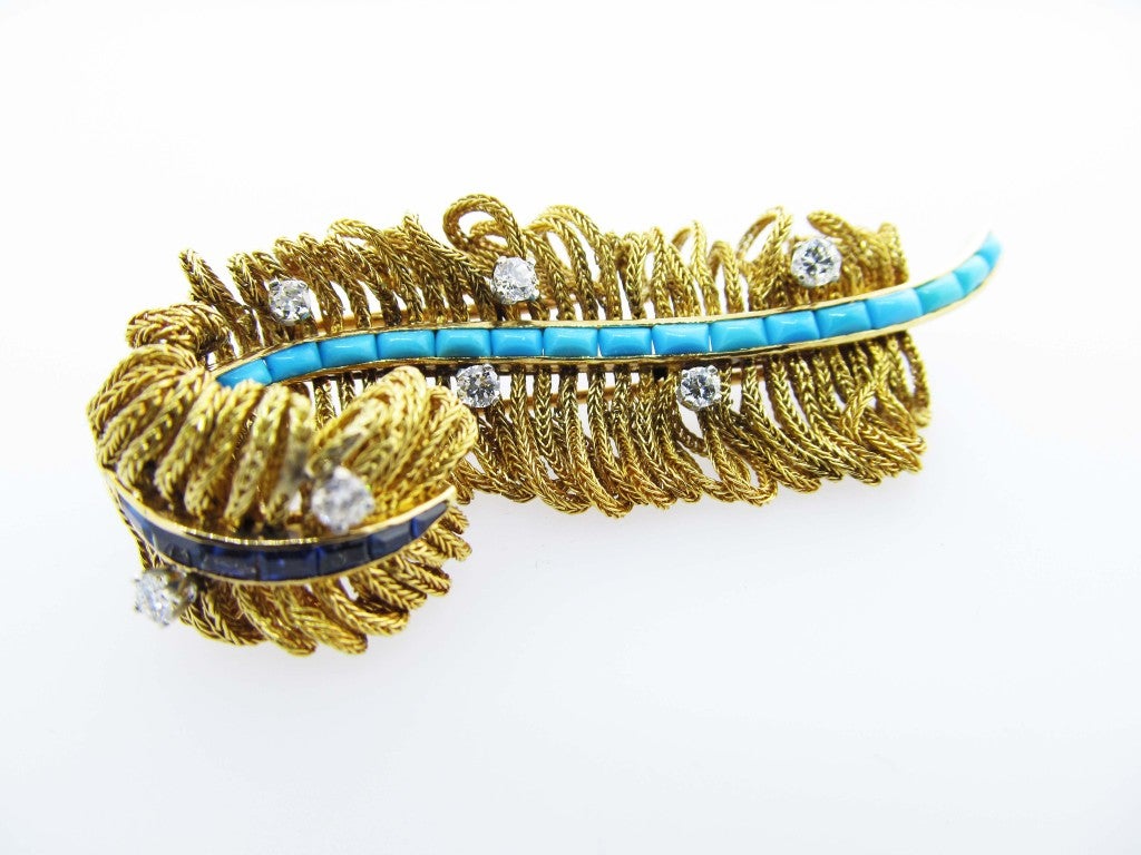 18kt. yellow gold feather double clip back brooch. The sides are edged with articulated loops of gold chain, lots of movement and dimension.
The center is channel set with sugarloaf cut natural turquoise and at the curved top with 7 channel set