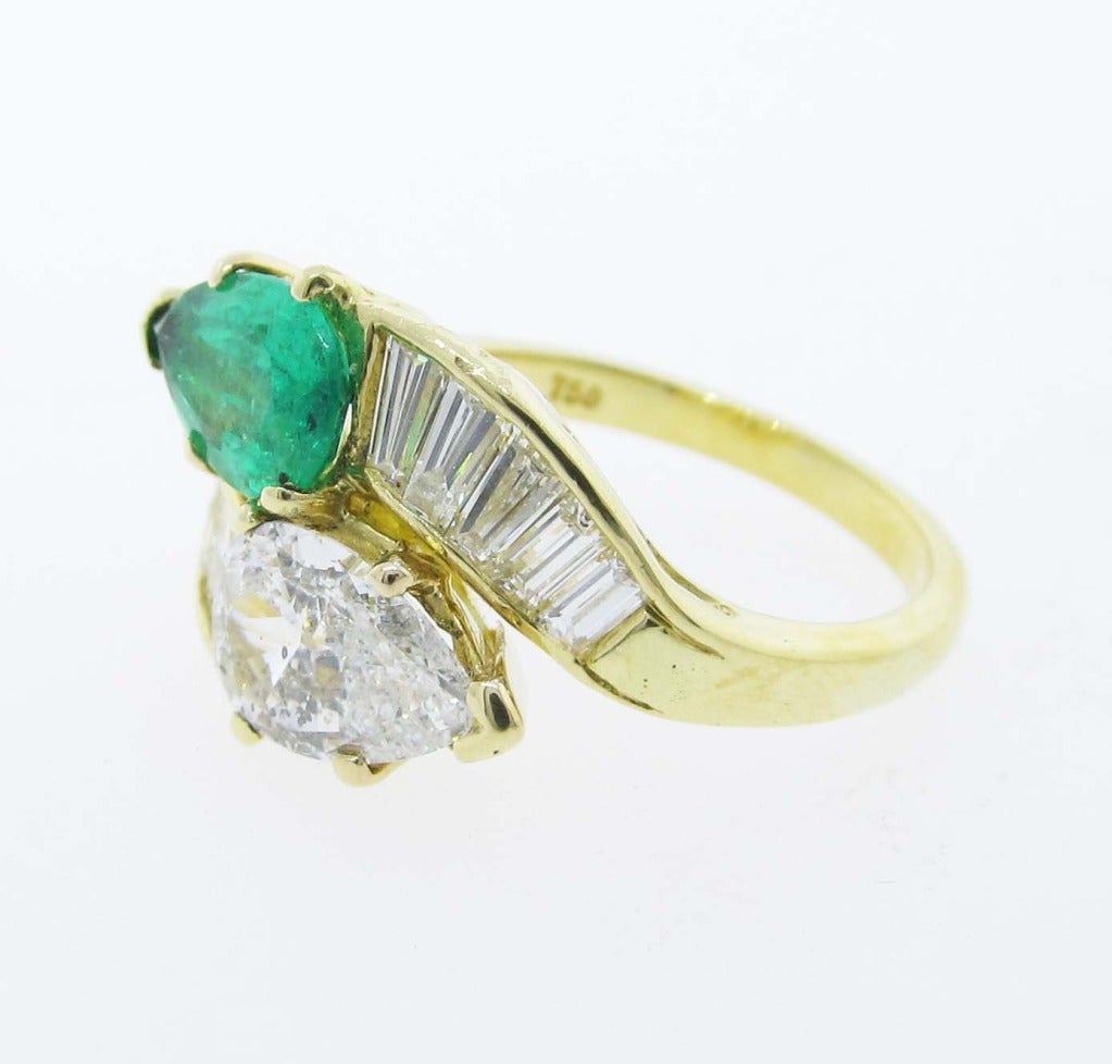 Custom made mount in 18kt yellow gold, the crossover design is prong set with a pear shape high color diamond weighing  approx.
.90cts. and a natural pear shape emerald weighing approx. .75cts. with 10 baguette cut diamonds on the shoulders