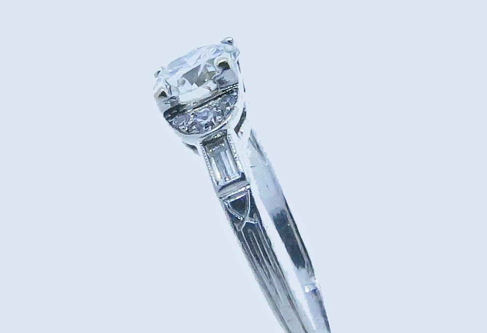 Detailed platinum mount diamond ring. Prong set with a center round European cut diamond weighing approx..80cts. grading VS clarity I color. The hand engraved mount is bead set with 3 round European cut diamonds and a baguette cut diamond on each