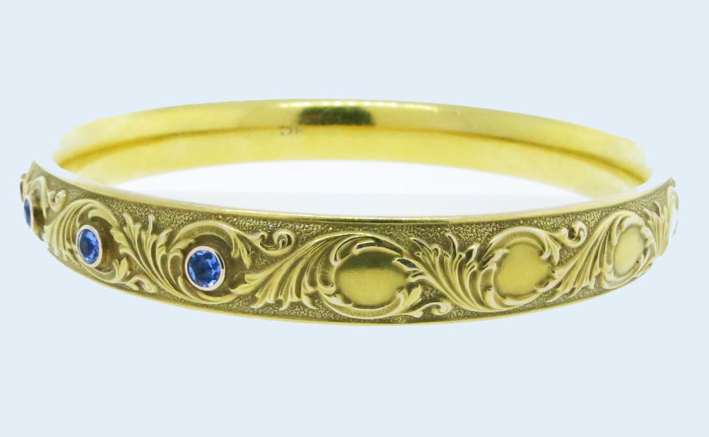 14kt. bloomed yellow gold repousse'  design slip on bangle bracelet. The top is bezel set with 7 round, natural, faceted cornflower blue sapphires totaling approx..80cts. The bracelet will fit the average wrist. Circa 1900. Excellent condition!
