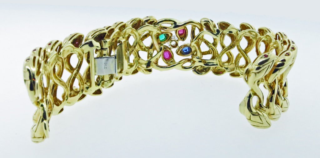 18kt. yellow gold hinged cuff bracelet. Each of the 18 snake heads are bead set with ruby eyes. The center is set with a round mine cut diamond weighing approx.45cts. Two cushion cut natural rubies, a cushion cut natural emerald and a sapphire. The