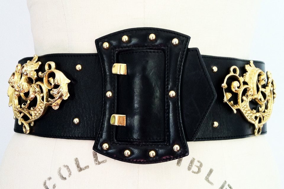 A rare vintage Bernard Perris 'Baroque' cinch belt. Wide black leather item with large gilt metal mounts. Item features two hidden snap closures behind a large matching leather covered faux buckle (will fit 30-31