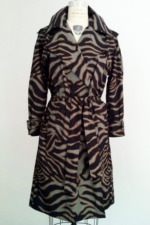 A fine and rare Yves Saint Laurent 'Safari' print trench wrap coat dress. Dynamic cotton print item worked up as a trench coat dress for I. Magnin. Item features a button front with matching fabric sash belt.