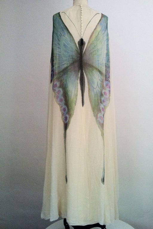 A fine vintage Mollie Parnis 'butterfly' gown ensemble. Large hand painted butterfly covers back of a silk chiffon flowing cape. Cape covers a matching ivory silk sleeveless gown. Gown fully lined and zips up back. Cape features a row of matching