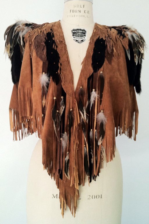 A fine and vintage artisan leather and fur cape. Signed hand cut suede leather item features authentic mink fur tails and assorted feathers, crystal and metal. Item features exaggerated shoulders, appliqued contrasting suede details and an open