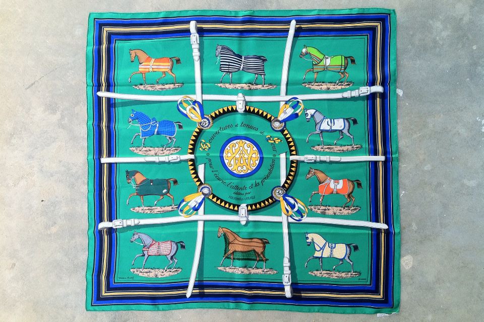 A stunning vintage Hermès 'Couvertures et tenues de jour' silk scarf. The scarf was originally designed by Jacques Eudel in 1962, and was reissued in 1974. The scarf is made from green silk and is printed with ten horses in different colours wearing