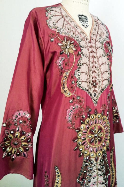 A fine vintage 'jeweled' kaftan. Elaborately decorated item features applique, embroidery and sewn on 'jeweled' techniques. 'Wine' to gold rayon sharkskin fabric item slips over head (no closures).