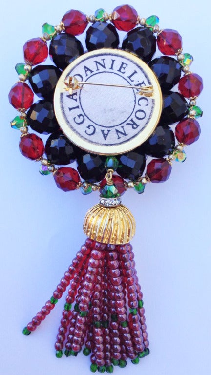 A exquisite and rare vintage Daniele Cornaggia brooch. Signed hand constructed gilt metal, glass and crystal item features authentic garnet beaded tassel. Original pin back intact.
