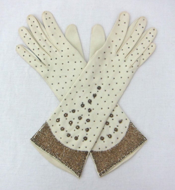 Featured is an elegant pair of dress gloves from the 1940s. Made of soft beige cotton sewn with gold seed beads. 

