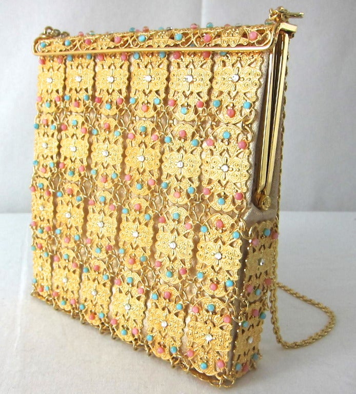 This is a glorious and different handbag! It is made of linked Gold metal filigree metal panels  imbedded with coral pink and turquoise  colored cabochons and rhinestones. It has hinge closure , interior pocket and chain strap. i-phone fits.  
