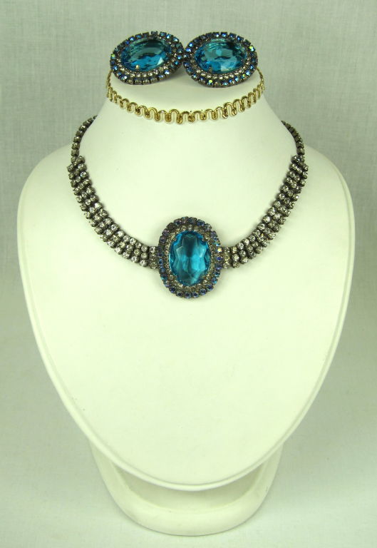 Fabulous necklace choke and clip on earrings set.  It has a big Aqua stone surrounded by rhinestones and another round of a darker blue. The neck is made of 3 rows of rhinestones and graduates to one. So wonderful for that special evening!
