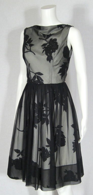 Featured is a beautiful dress of printed taffeta with chiffon overlay and a dramatic shoulder sash in back. The taffeta has a large black floral motif against a very light gray background. The bodice is fitted and features a slight cowl neckline.