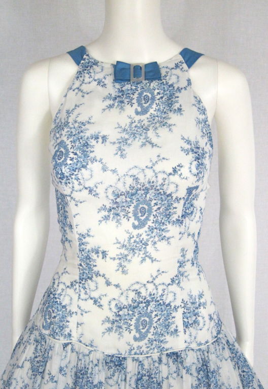 Featured is a beautiful blue and white printed summer dress by Miss Cane of New York. The cotton is printed with a delicate floral and paisley motif against a white background. The halter-style bodice is fitted and trimmed with a small sateen bow at
