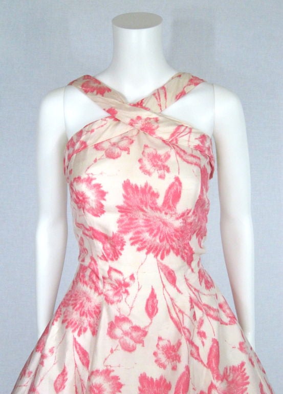 Featured is the prettiest pink and white floral dress by Suzy Perette of New York, from the 1950s. The raw silk features a motif of hazy pink blooms against an oyster-colored background. The halter bodice has crossover straps that connect to a low