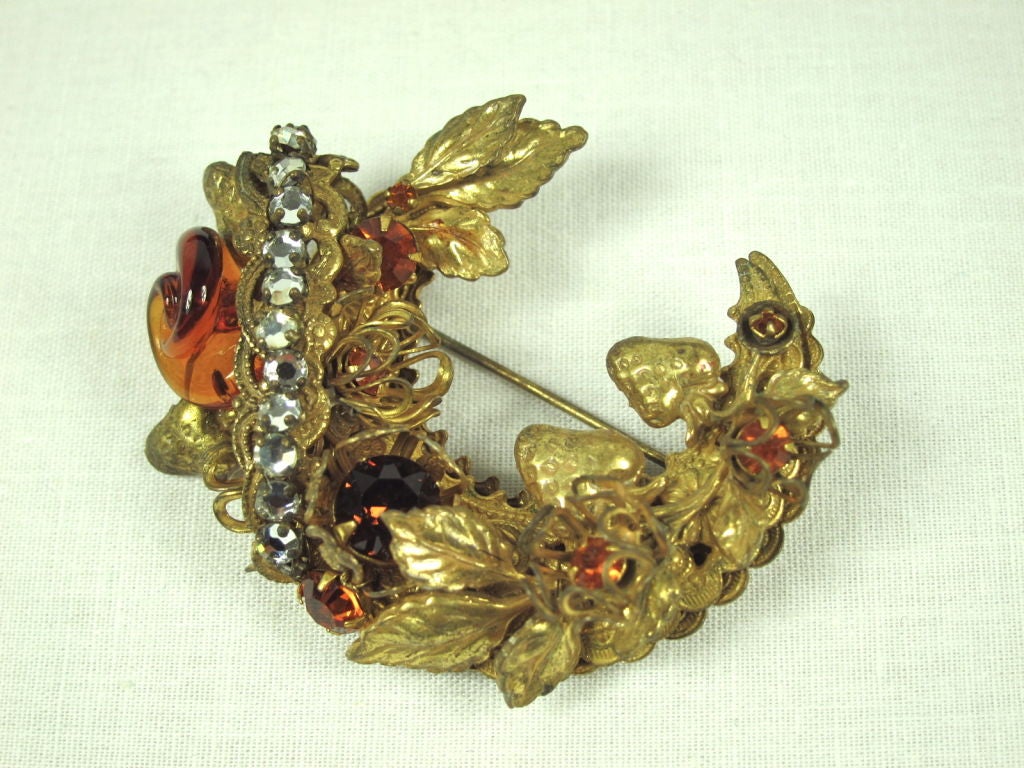 Featured is an intricate brooch by Miriam Haskell from the 1950s-1960s. It has a multitude of details including strawberries and leaves, prong set rhinestones, molded glass rosette, and wire flowers. It fastens with a pin backing. This is a