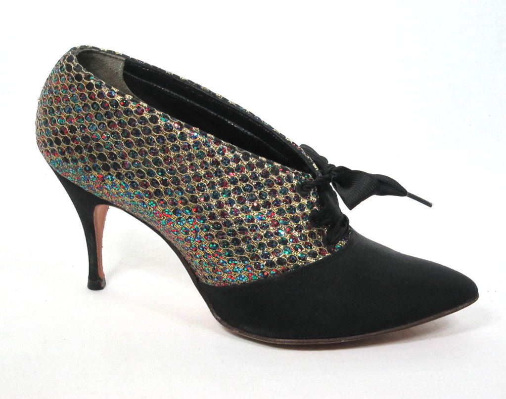 Featured are fabulous pair of party shoes from the 1950s by Coccini. The upper portion is embellished with gold lace and rainbow glitter for a sparkling snakeskin look. Black faille makes up the stiletto heel and pinty toe. The original twill ribbon