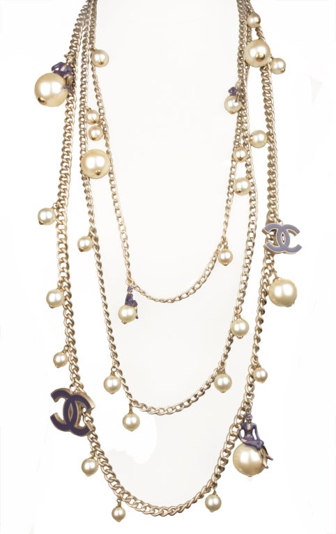 This is a  whimsical Chanel multi stand necklace with figures of Coco sitting atop large pearls. The figure and logo are in purple enamel. The largest pearl measures 1 