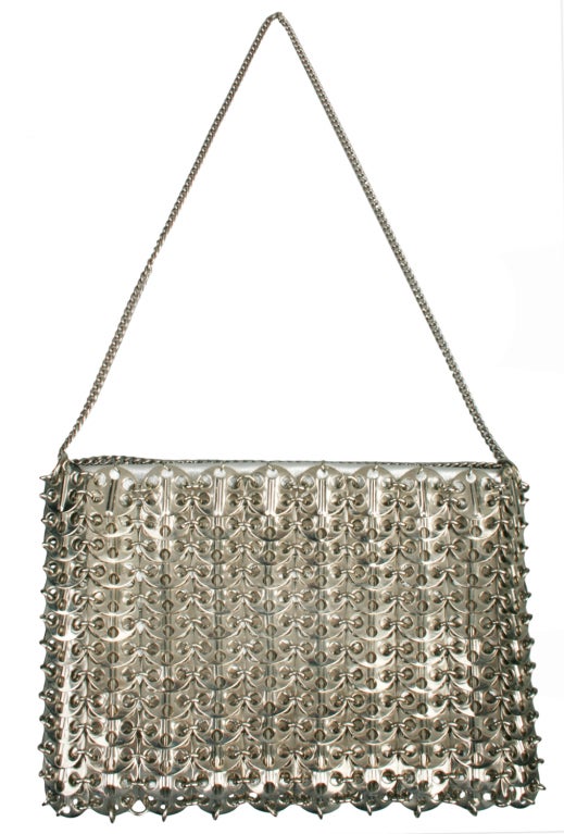 A metal mesh handbag of interlocking aluminum discs attached to silver lame' leather. The inside compartment is lined with ivory colored fabric. 
The drop length of the strap for shoulder use is 11