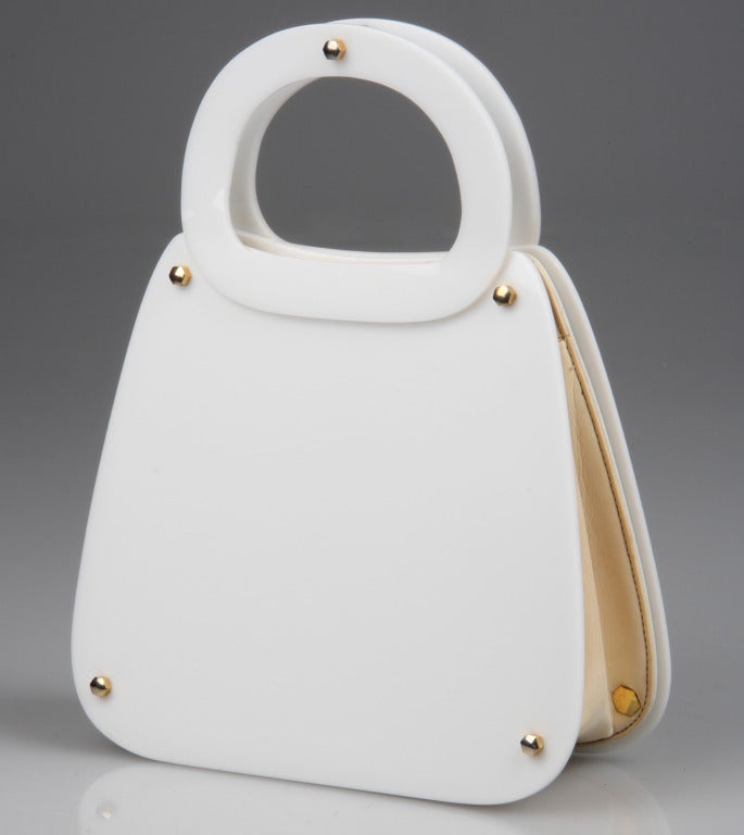 This is a chic,  contemporary and fresh handbag with vintage charm. Made by Koret, the front and back as well as the handles of this bag a  made of white Lucite.
Trimmed with gold  toned hardware, the lined bag has two side pockets, one being