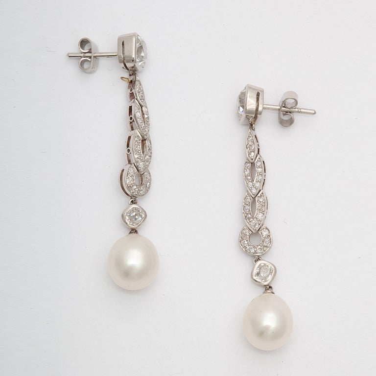 Pair of natural pearl earrings, in pavé platinum and diamond settings.