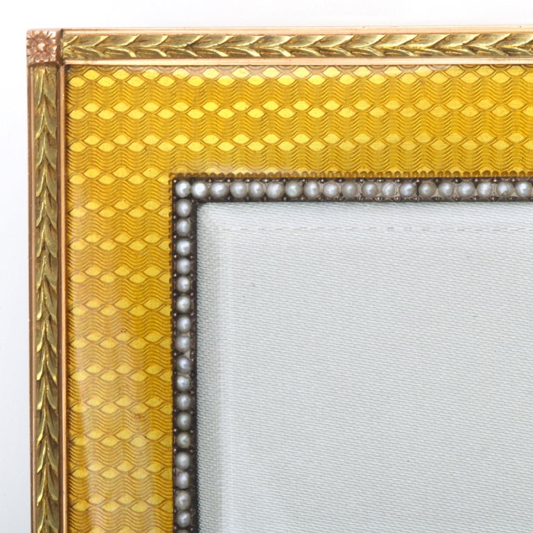 Gold and yellow translucent enamel frame with an inner border of  seed pearls around the aperture and the outer border with chased gold laurel leaves, accented by rosettes.
Workmaster, Michael Perchin. 
Dimensions: 3-7/8 x 2-1/2 in.; Aperture: