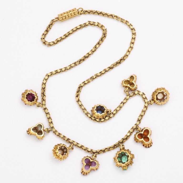 Gold archaeological revival style necklace with nine different clustered stone pendants.

The stones, from left to right, are sapphire, yellow sapphire, white sapphire, citrine, emerald, amethyst, pearl, chrysoberyl cat's eye, and