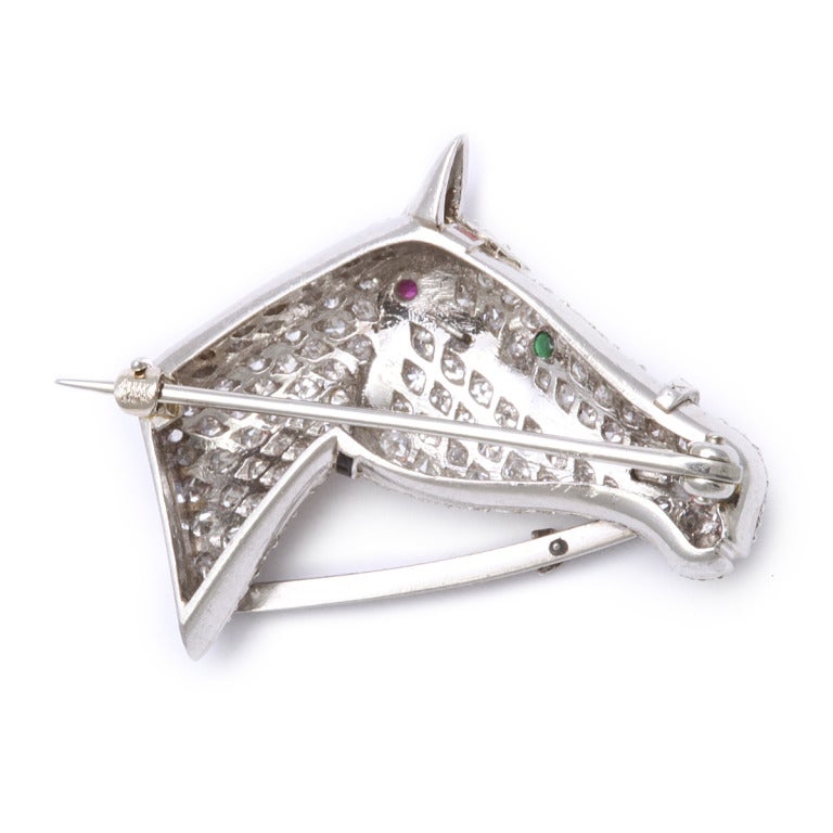 Pavé diamond set horse head brooch in platinum with a black enamel bridal, a ruby and white enamel headband and an emerald eye.