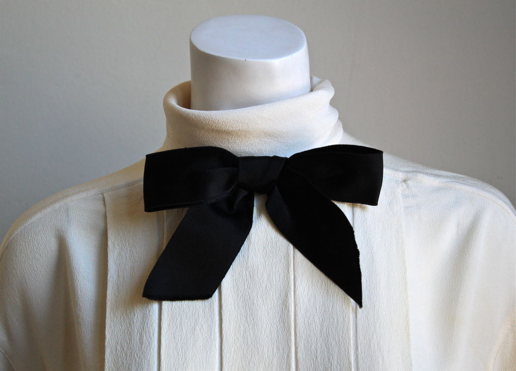 Classic off-white silk blouse with pintucks and black bow at neckline from Chanel Boutique dating to the 1980's. Fits a US 6-10. Buttons up the back. Made in France. Very good condition (cuff links are missing - those pictured are not included).