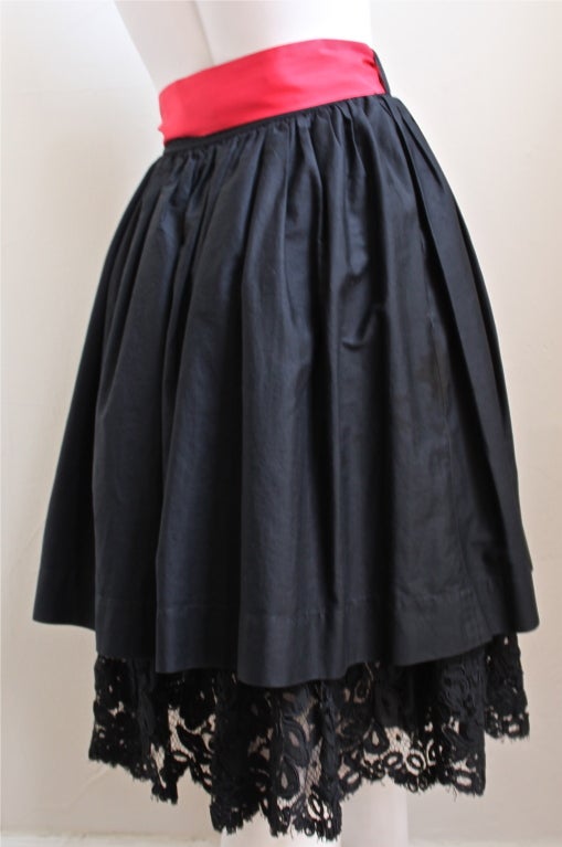 Black cotton skirt with lace petticoat and red satin sash from Yves Saint Laurent dating to the early 1980's. Labeled a French size 40, although this skirt best fits a 24-25