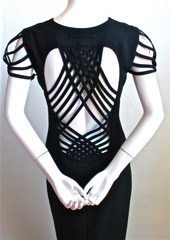 Very unique jet black gown with intricately woven back detail from Jean Paul Gaultier. Woven, cutout design on cap sleeves and back creates architectural cage effect. Straight silhouette with clean lines. Mini train in back. Labeled a French 38/