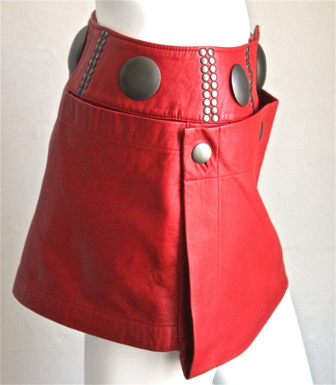 Vivid red leather mini skirt with gunmetal oversized studs from Issey Miyake dating to the 1980's. Labeled a size medium however this skirt best fits a size small or medium. Approximate measurements: 28