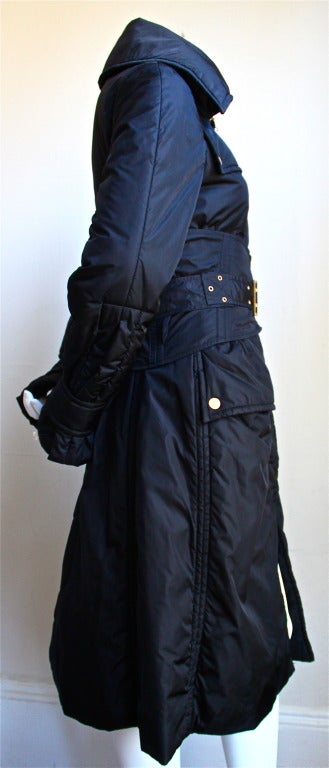 Jet black insulated nylon trench coat with black corset belt designed by Tom Ford for Gucci as seen on the runway Fall 2003. Labeled an Italian size 42. Approximate measurements: bust 34”,  shoulders 14.5”, waist 25-27” (belted), and overall  length