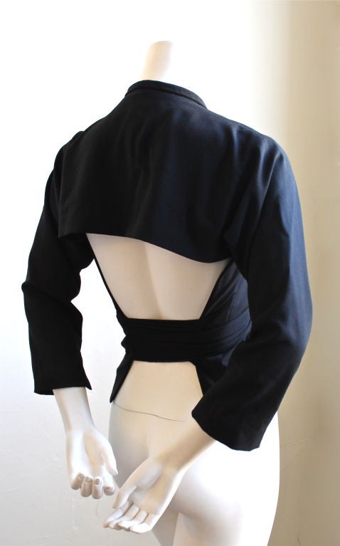 Unique lightweight black wool jacket with open back from Issey Miyake dating to the 1990's. Best suited for a size small. Two button closure. Cropped arms with slits a wrists. Tie can be worn in front or back. Made in Japan. Excellent condition.