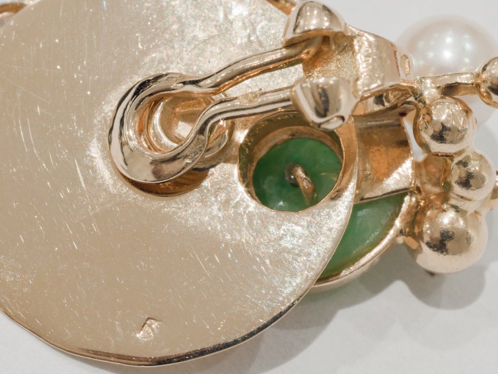18kt gold earclips of circular gold disc surrounded by emerald, jade, diamond, and pearl accents. 