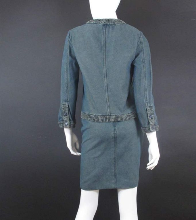 Chanel 'pre-washed' blue denim suit comprising jacket, bustier and skirt.  The jacket has a round neckline, five button closure, four welt pockets and 3/4 sleeves with two buttons on each cuff; pleated fabric trims the neckline, front, pockets, hem