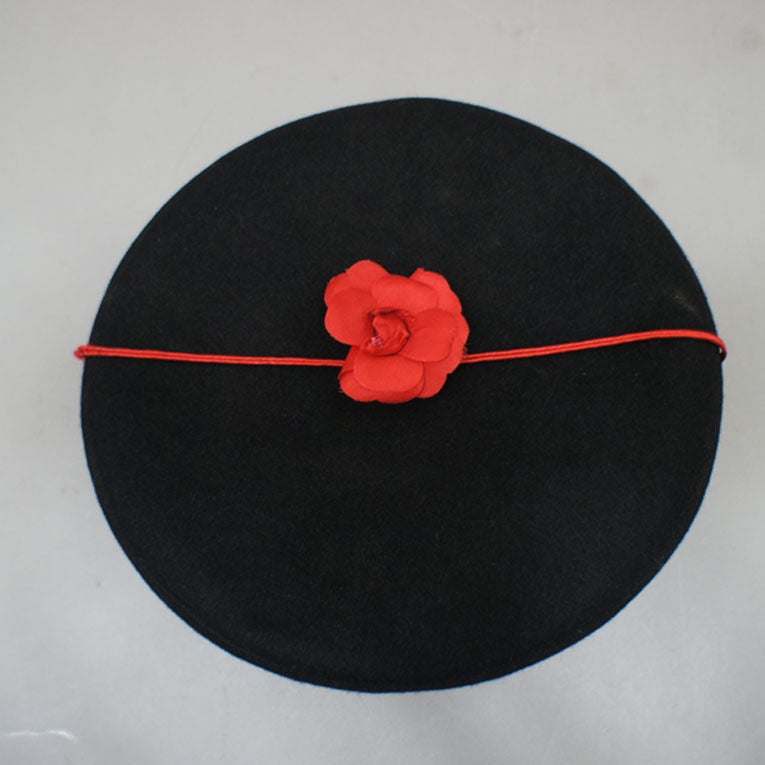 CHANEL beret in black furfelt with stitched red CHANEL typography across front. Signature red silk camelia sits upon the top (connected with a red striping band). Highly collectible, très chic item. <br />
<br />
Fabric: 100% Furfelt<br