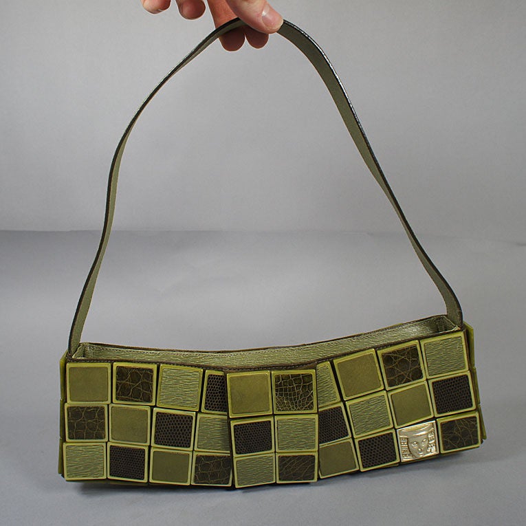 Kieselstein Cord Woman of the World bag in olive green. This gorgeous bag is part of a series that features unique tiles on the exterior of the handbags with the gold tile marking as part of the 'woman of the world' series. The bag is slightly