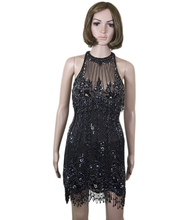 This show-stopping Bob Mackie features an intricate beaded vine and floral design. With a sheer mesh bust, a shoulder-baring racerback, and a figure hugging silhouette, this sexy cocktail dress sparkles with rhinestones, black sequins, and bugle