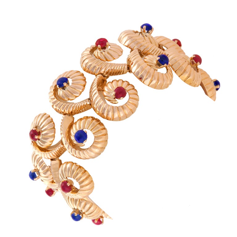 A French Mid-20th Century 18-karat gold bracelet with rubies and sapphires. The bracelet has 10 cabochon rubies with an approximate total weight of 1.80 carats, and 12 cabochon sapphires with an approximate total weight of 2.16 carats. The bracelet