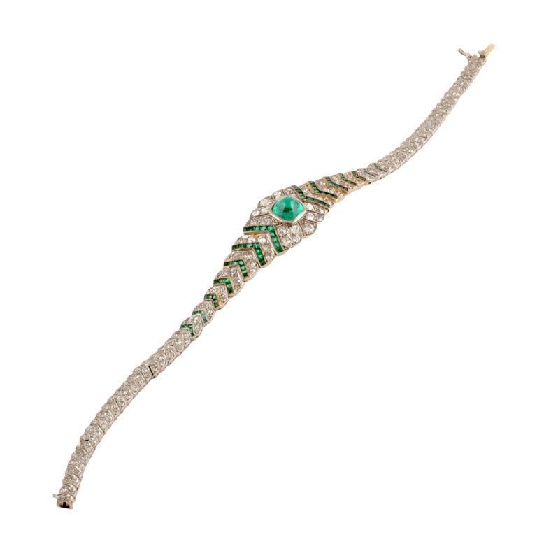 An Art Deco platinum, diamond and emerald bracelet. The bracelet centers on a sugar loaf emerald that has an approximate weight of 1.25 carats and is surrounded by round diamonds and calibre-cut emeralds tapering down the wrist in a chevron motif.