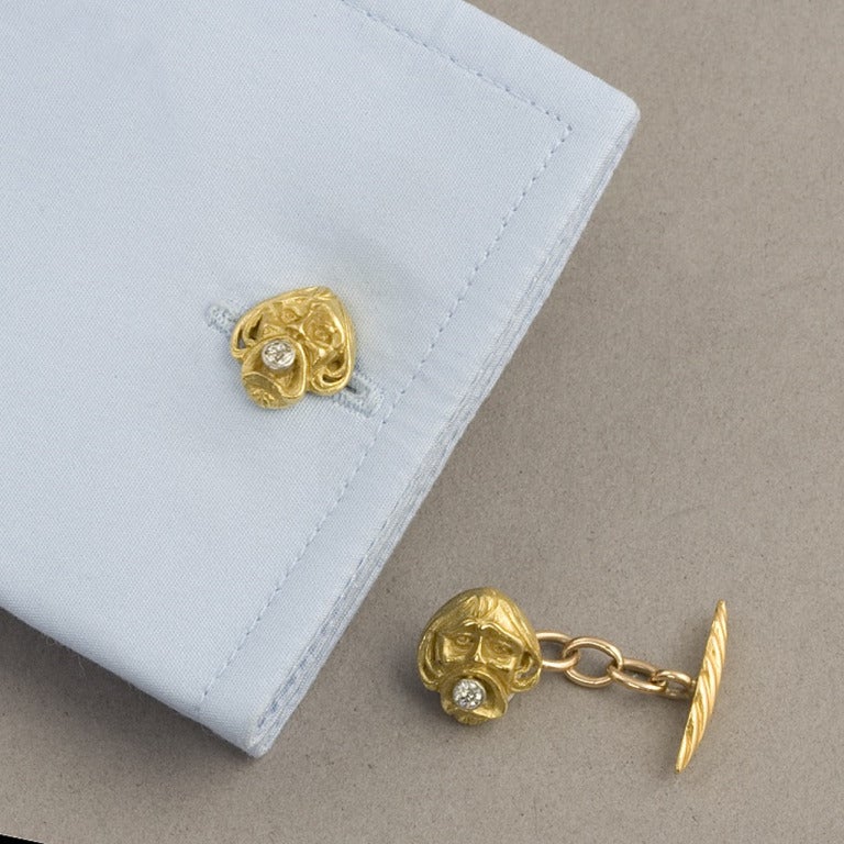 Art Nouveau gold and diamond cufflinks. The 18-karat gold cufflinks feature a carved face on one side with an Old Mine-cut diamond in his mouth, altogether totaling approximately .20 carat, and a ridged gold oval bar on the other. Circa 1900.

(MG