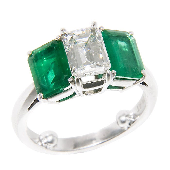 Platinum 3 Stone ring set with an Emerald step Cut Diamond weighing 1.47 Carat, grading as I color and SI Clarity, Flanked on either side by an Emerald Step Cut Emerald each measuring 7 X 5 M.M. and having deep Rich Green color possibly of Columbian