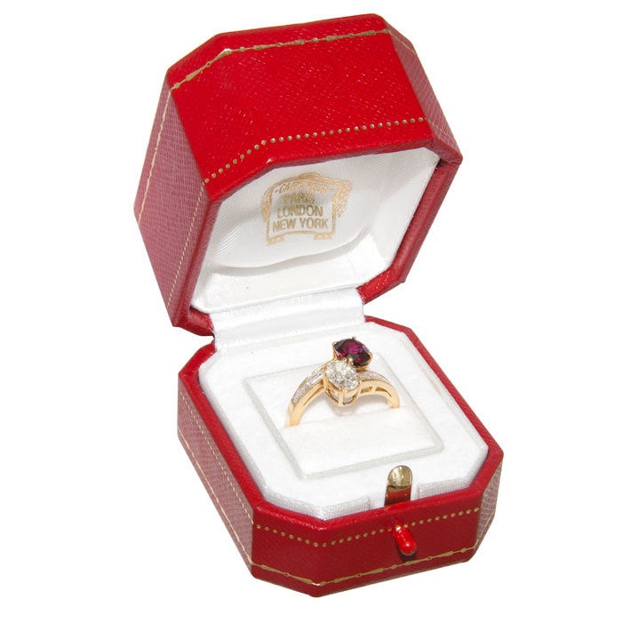 18K Yellow Gold Bypass Ring by Cartier, set with a .75 Carat Oval Diamond that is G in Color and VS in Clarity and a 1 Carat Oval Ruby of Fine Color Possibly Untreated, further set with Square and Baguette Diamonds. Stamped and Numbered.Finger size