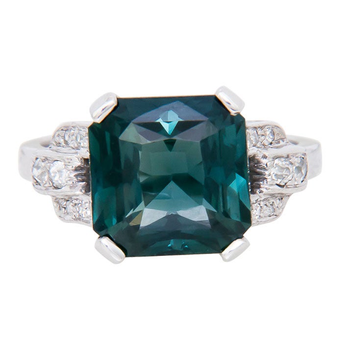Circa: 1940 Platinum and Diamond Ring, Centrally set with an old Stepped cut Green Ceylon Sapphire.  Weighing 6.50 Carats and Showing some hues of Blue-Purple. Finger size =6