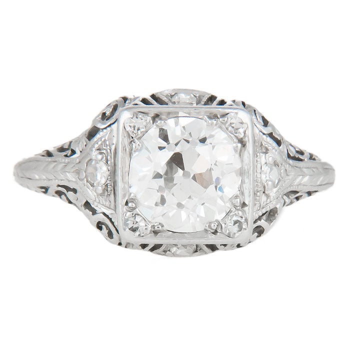 Circa: 1920s Platinum and Diamond Engagement Ring, centrally set with a 1.35 carat Old Mine Cut Diamond that is I in Color and SI in Clarity. The Mounting is further set with smaller Diamonds and features very fine Gallery work and Engraving. Finger