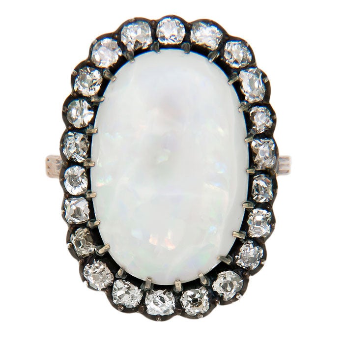 Circa: 1900 Silver top and Yellow Gold shank ring, centrally set with a natural Opal, approximately 6 to 8 carats and showing more white with lots of flecks of red, blue and green. The opal is surrounded by approximately 1.25 Carats of Old Mine cut