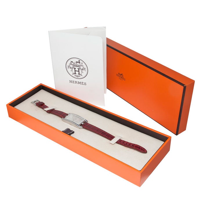 Never worn Hermes lady's stainless steel dual time zone wristwatch, Cape Cod. Quartz movement, two setting crowns, silvered dial, burgundy textured strap. Comes with instruction manual, guarantee papers and original box. With factory plastic on the