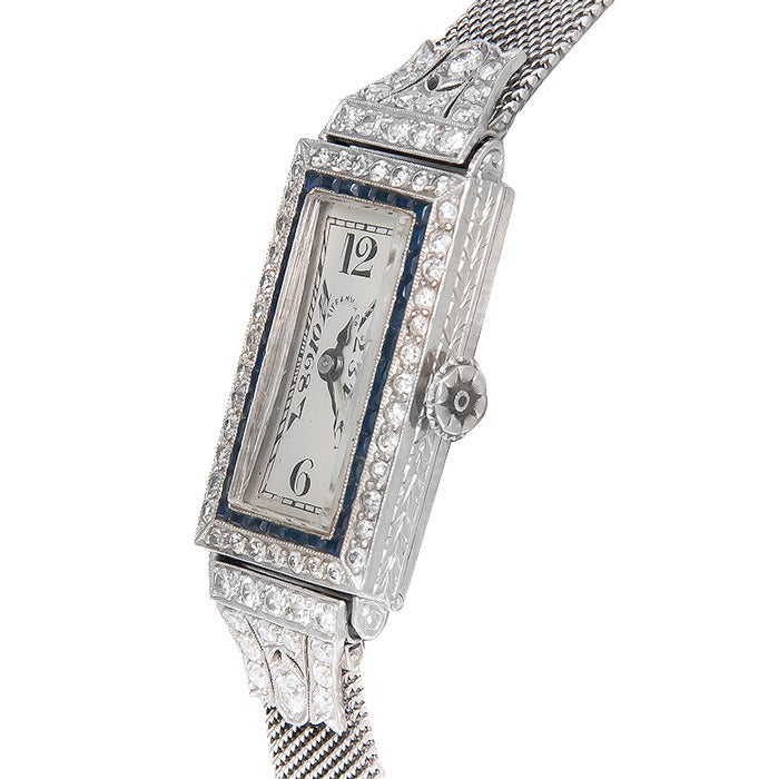 Patek Philippe lady's platinum, diamond and sapphire wristwatch, retailed by Tiffany & Co. circa 1920s, in a platinum contract case. Silvered dial with Arabic numerals, 18-jewel manual-wind movement. Baguette sapphires and diamonds set around the