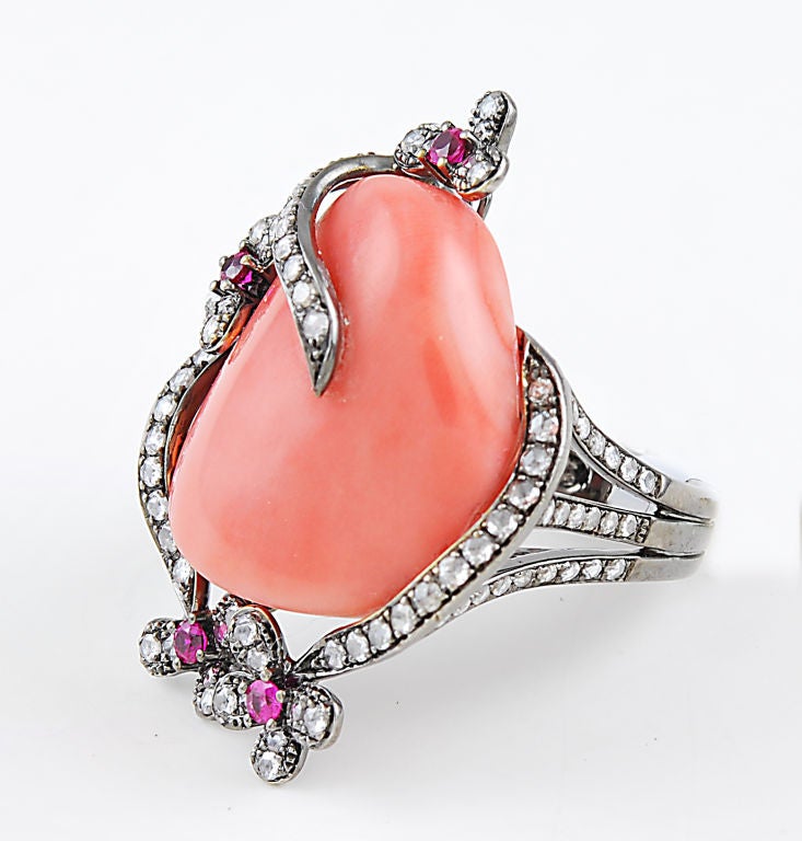 A large nugget of sunny coral captured by tendrils of white gold embellished with diamonds and flowers centered with rubies.  This ring is a size 7, but is easy to size.