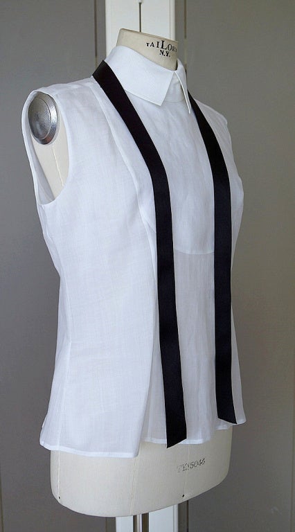 Guaranteed authentic  CHANEL 03C  fabulous tuxedo top. 
Crisp white sleeveless top with a tuxedo bib front center.
Higher cut collar with a black satin ribbon that loops through the rear of the collar.
Can be worn open or tied as you